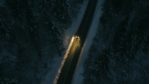 Aerial shot of a car driving next to a icy forest at night.