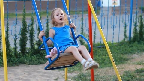 Sad child girl swings on the playground