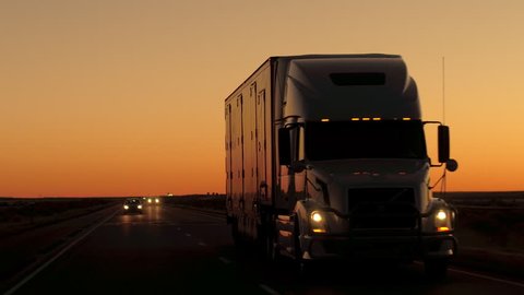 CLOSE UP: Freight container semi trailer truck transporting goods. Cars on road trip driving along the beautiful country highway after the sunset. Lorry shipping cargo, people traveling by night