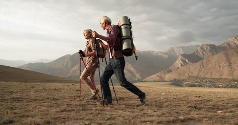 Old caucasian couple hiking, trekking in mountains with backpacks, enjoying their adventure - tourism concept 4k