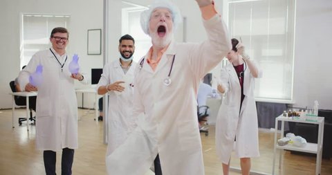 Crazy happy doctors dancing in the clinic. Three male doctors and a nurse have fun resting in the workplace during a break. Friendly cheerful doctors