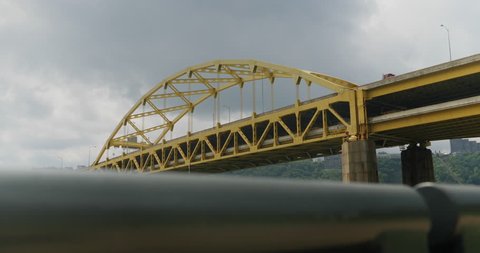 A daytime dolly up establishing shot of the iconic yellow Fort Duquesne Bridge over the Allegheny River in downtown Pittsburgh, Pennsylvania on an overcast summer day.  	