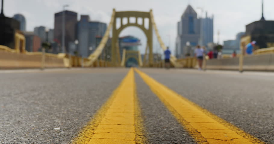 A low angle slow dolly tracking shot of the bridgedeck of the Roberto Clemente Bridge in downtown Pittsburgh, Pennsylvania. City skyline in the distance.  	