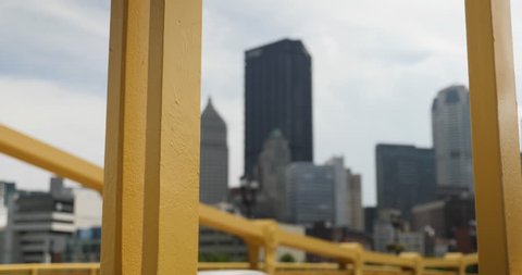 A daytime tracking dolly shot of the Pittsburgh skyline as seen through the yellow steel beams of the Andy Warhol Bridge.  	