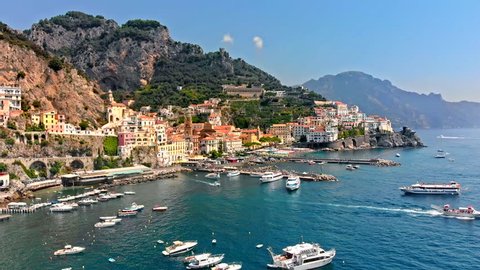 Flying along the old town of Amalfi coast passing a waterway shore port, docks and boats Italy. Aerial drone view