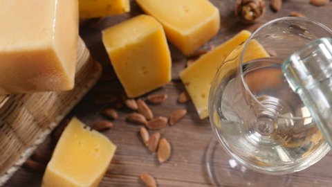 Wine and cheese. Food art. Different sorts of hard cheese beautifully surved on a wooden background. White wine is being poured into wine glass.