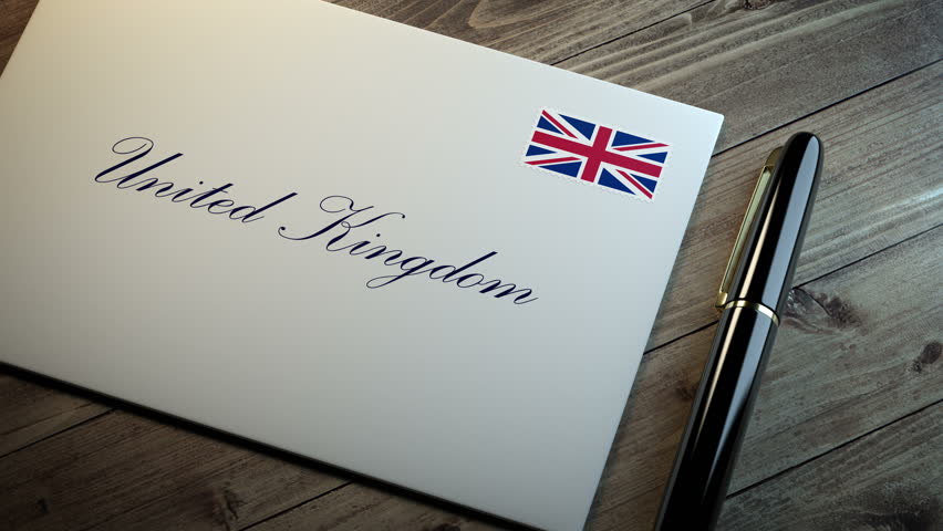 Country name written on a card or envelope in cursive font with a sleek pen on a wooden table surface under beautiful classy light. Stamp in the corner shows the flag of United Kingdom