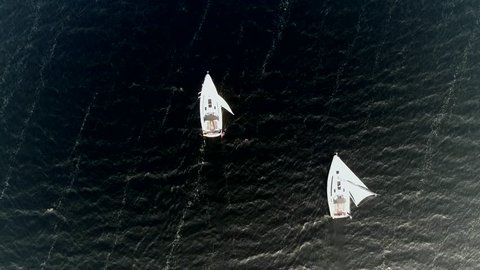 Aerial top down footage of two white sailboats sailing next to each other over dark ocean at night the vessels are propelled entirely by sails also showing heavy current in water 4k high resolution