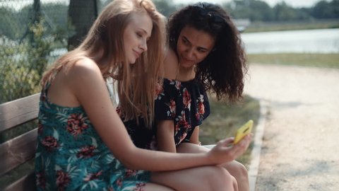 Two young girls using mobile phone while sitting on a bench.