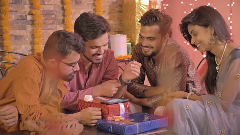 A young and happy group of friends in traditional costumes playing a game together on smartphone in interior house setup decorated with flowers and lights. A group of young people talking and smiling