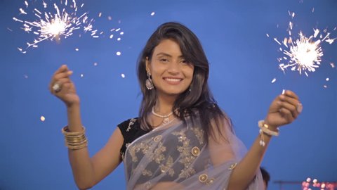 A Young and beautiful woman in a traditional sari playing with fire sparkle or firecracker. Slow motion shot of an attractive and smiling lady playing with fireworks outdoors during Diwali Festival