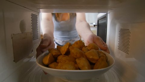 View from microwave oven young woman opens door and takes out dish with fresh delicious pies in kitchen
