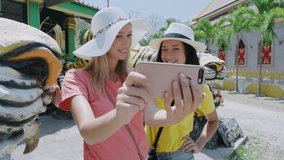 Young happy tourist woman doing selfie video / photo with smartphone at Asian buddhist temple entrance in Thailand south east Asia. Slow motion travel technology concept. 