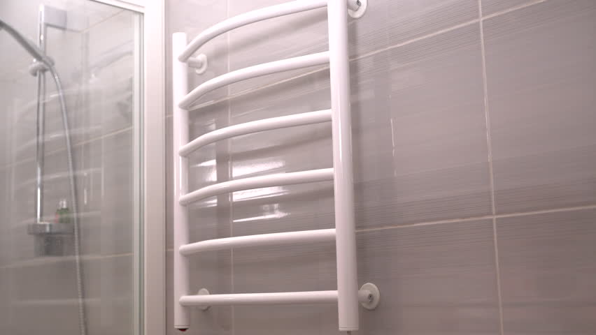 Woman hanging a towel on a wall mounted towel rack on a tiled bathroom wall smoothing the soft cotton with her hand