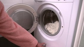 Woman placing dirty laundry into a front loading a washing machine then closing the door once it is full