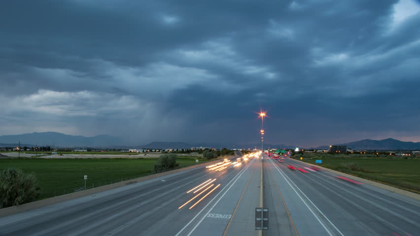 Time lapse of traffic driving on highway in the evening as storm and lightning pass through the valley.