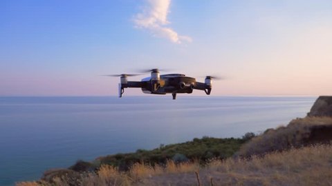 Quadrocopter flies to the camera on the background of the sea at sunset. UAV flights in slow motion (120 fps).