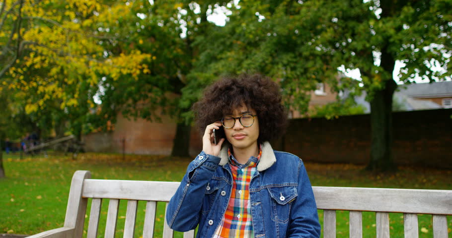 4K Zoom in to close up of young man having a phone conversation in the park. Slow motion.