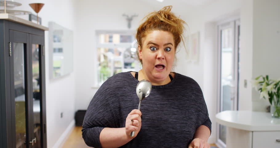4K Funny overweight girl dancing & singing into a spoon in the kitchen at home. Slow motion.