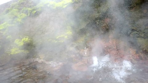 Steam geyser closeup in Deildartunguhver hot springs in Iceland with cloudy mist fog coming out of red rock colorful cave boiling water vapor