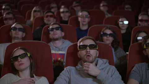 Spectators in 3d glasses watching film in cinema. People watching film at movie theatre. 3d movie audience. People in 3d glasses at movie hall in slow motion