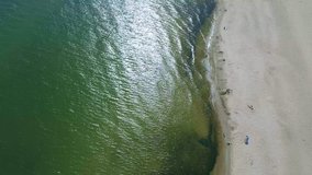 4K. Aerial view on the green ocean with a sandy beach. Summer sunny day, people went out to sunbathe on the beach.