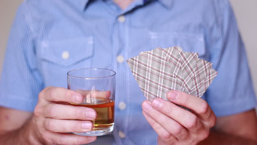 Holding whisky and playing cards in hands