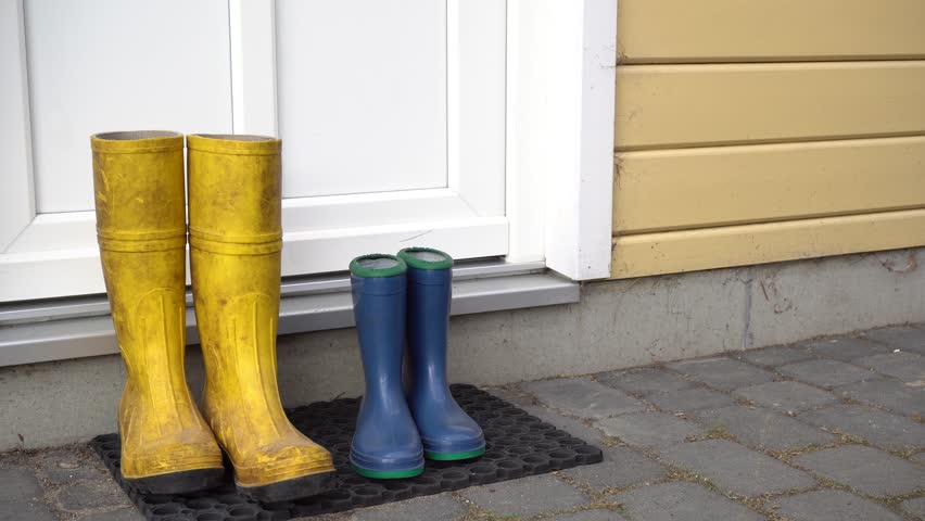 Two people get into blue and yellow rubber boots in front of the house