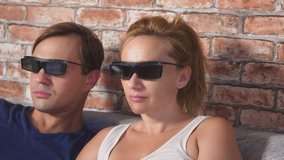 Close Up. a young couple in glasses 3d, sitting on the sofa in the living room with many emotions, watch the movie. 4k, slow motion.