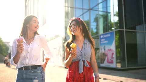 Two young female friends having fun and eating ice cream. Cheerful caucasian women eati icecream outdoors walking in the city. Pretty girls posing with ice-cream. Summer time concept. Slow motion