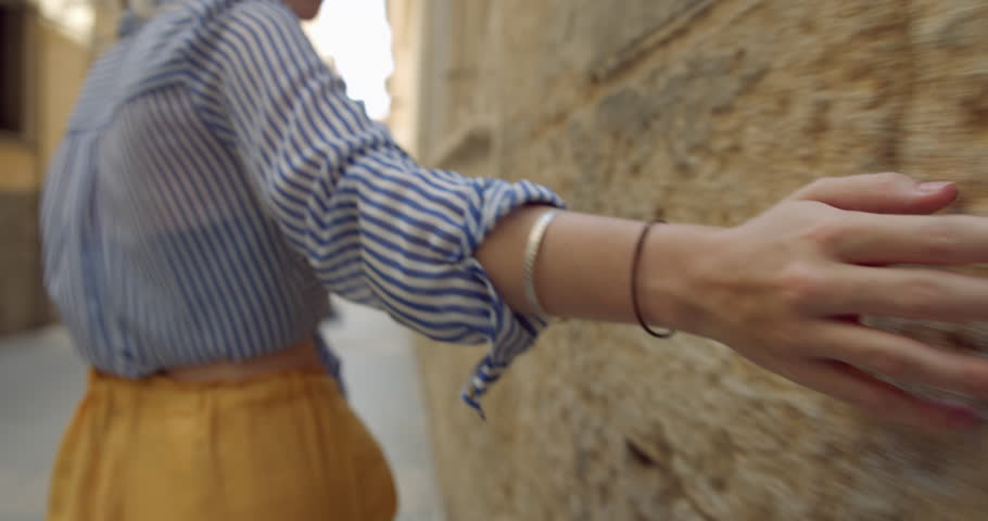 Young Pretty Blonde Woman Tracing Fingers over Spanish Old Town Wall, Girl Exploring a Brick Building Ston in Spain. A Tactile Tourist Traveller on Holiday in Spain.
