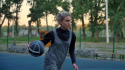 Beautiful young woman playing basketball and failing, ball missing hoop, practicing in park during morning