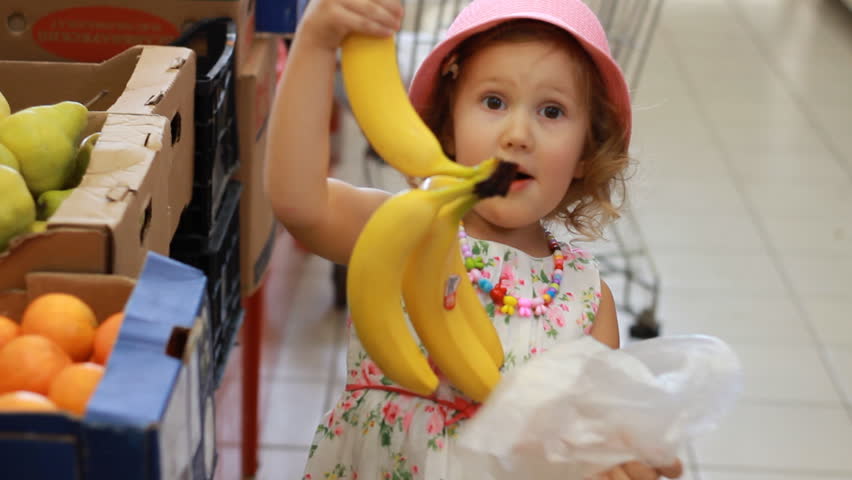 Bananas. Child girl in the store chooses fruit. Grocery supermarket and shopping trolley