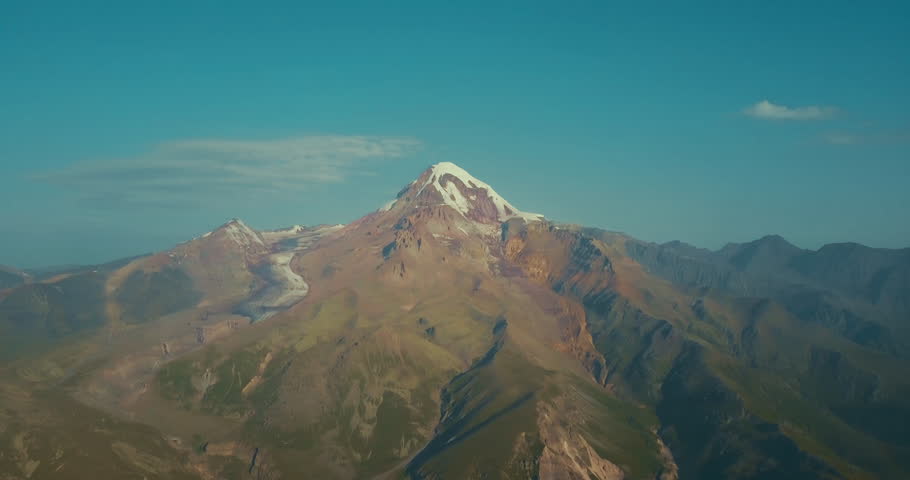 Drone footage of mount Kazbek with an altitude of 3,500 meters, camera making pano, eternal glacier on top, gorges and traces of melting flows on the sides, mountain ranges opposite Kazbegi, Georgia Royalty-Free Stock Footage #1015299898