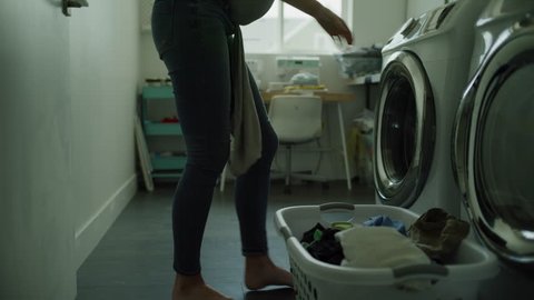 Multitasking mother carrying baby and loading clothing into washing machine / Lehi, Utah, United States