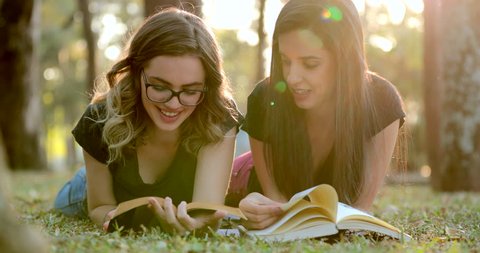 Girls lying on grass reading books in the sunlight outdoors. Campus students together studying outside Stockvideó
