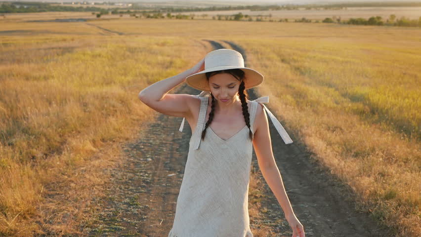 girl in the hat and dress is on the field at sunset on the track