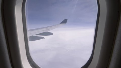 POV, CLOSE UP: Unknown person pulls up airplane window shade and reveals a stunning view of the bright blue sky. Looking through small window at wing of commercial airplane cruising at high altitude.