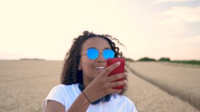 Slow motion follow shot video of beautiful mixed race African American girl teenager young woman in white T-shirt and blue sunglasses walking using her smart cell phone