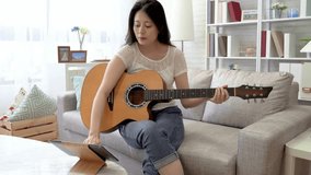 Asian woman recording a video of herself playing the guitar. She will review the video and check the mistake and revision.