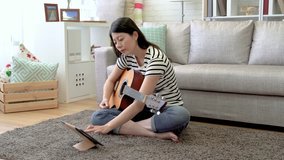 Asian underground music player recording the videos of she playing the wooden guitar in the living room. She wants to share with her fans online digital tablet.