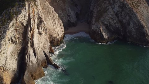 Ocean waves reaching shore crashing into rock formations. 4k drone footage dramatic shot