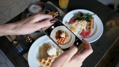 Female hands photographing appetizing food by smartphone in the restaurant.