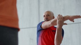 Low angle shot of unrecognizable yoga instructor teaching shoulder stretch exercise to senior man with grey hair and moustache standing opposite - Powered by Shutterstock - Get 15% off with code: PIKWIZARD15