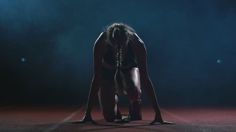 Professional woman athlete on a dark background gotovtes to run the sprint of Jogging shoes in sneakers on the track of the stadium on a dark background. Close up