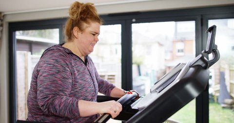 4K Obese woman trying to lose weight, struggling on treadmill & looking at camera. Slow motion.