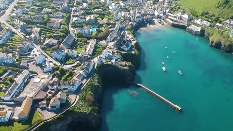 Port Isaac in Cornwall seen by air in sideways panning shot revealing the town, blue sea, countryside and fields beyond. Features vehicles and people moving around the town
