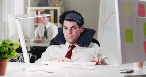 Sales manager waking up from snap in office, putting off sleep mask, yawning and starting working on his computer
