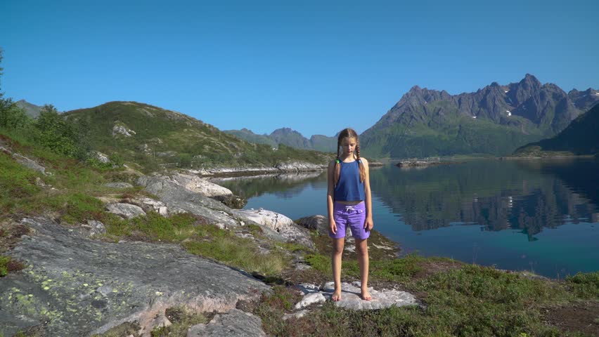 A happy girl is dancing against the background of the mountains and the sea bay. The beautiful nature of Northern Norway and the Lofoten Islands. 4K