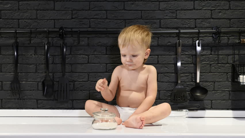 Cute baby boy sitting on kitchen table touching and tasting sugar and eating it. having fun. Having fun, smiling, laughing. 4k